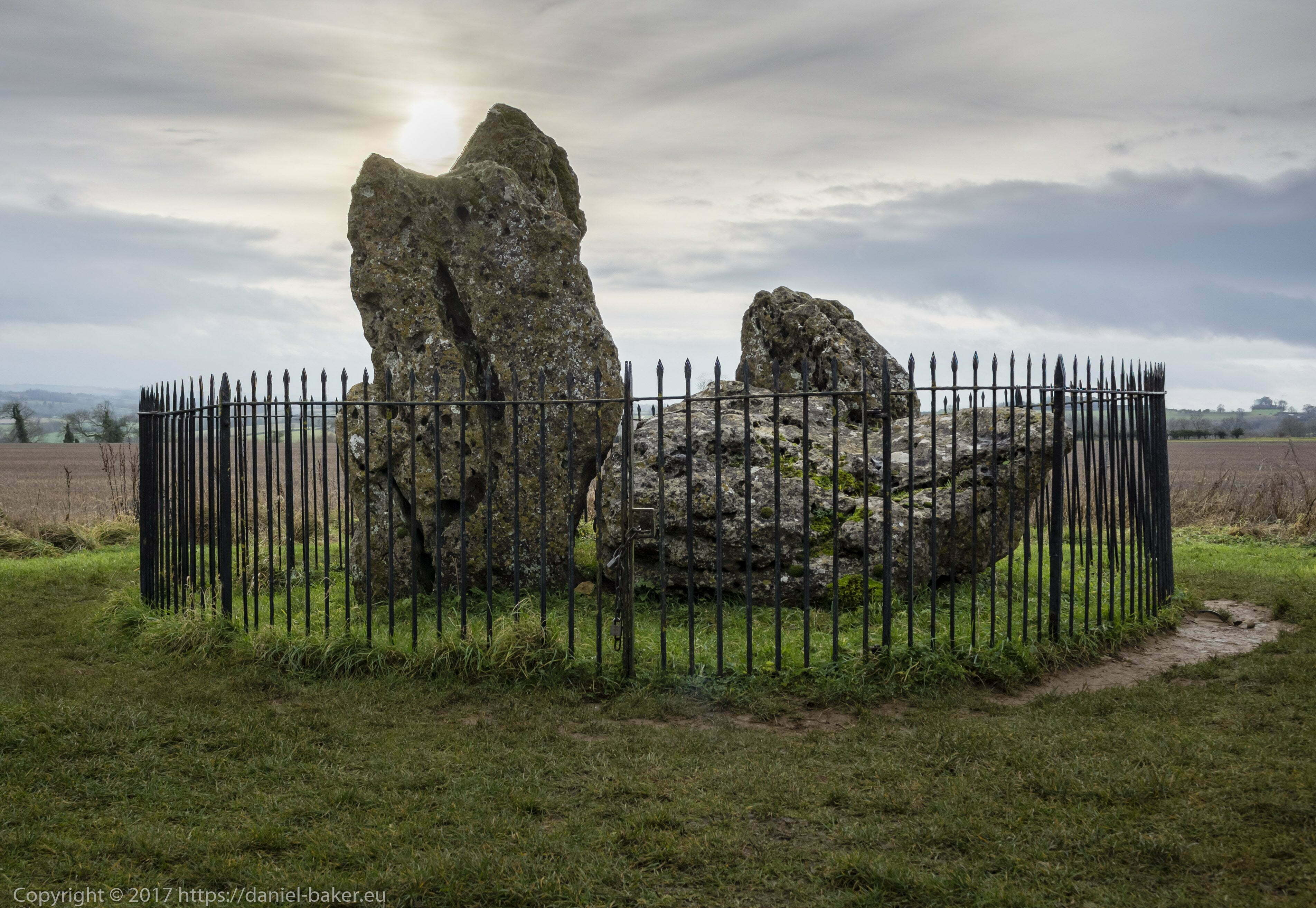Neolithic stones surrounded by black iron fence with the winter solstice sun shining above